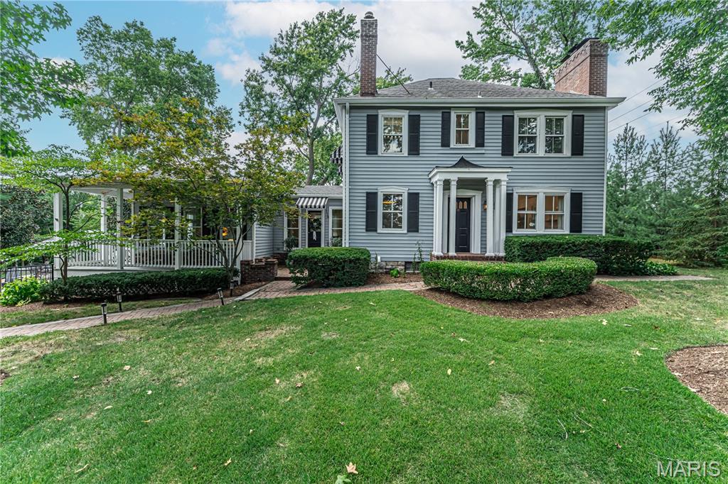 Two-story gray house with black shutters, white entry columns, and a covered porch beside a broad lawn.