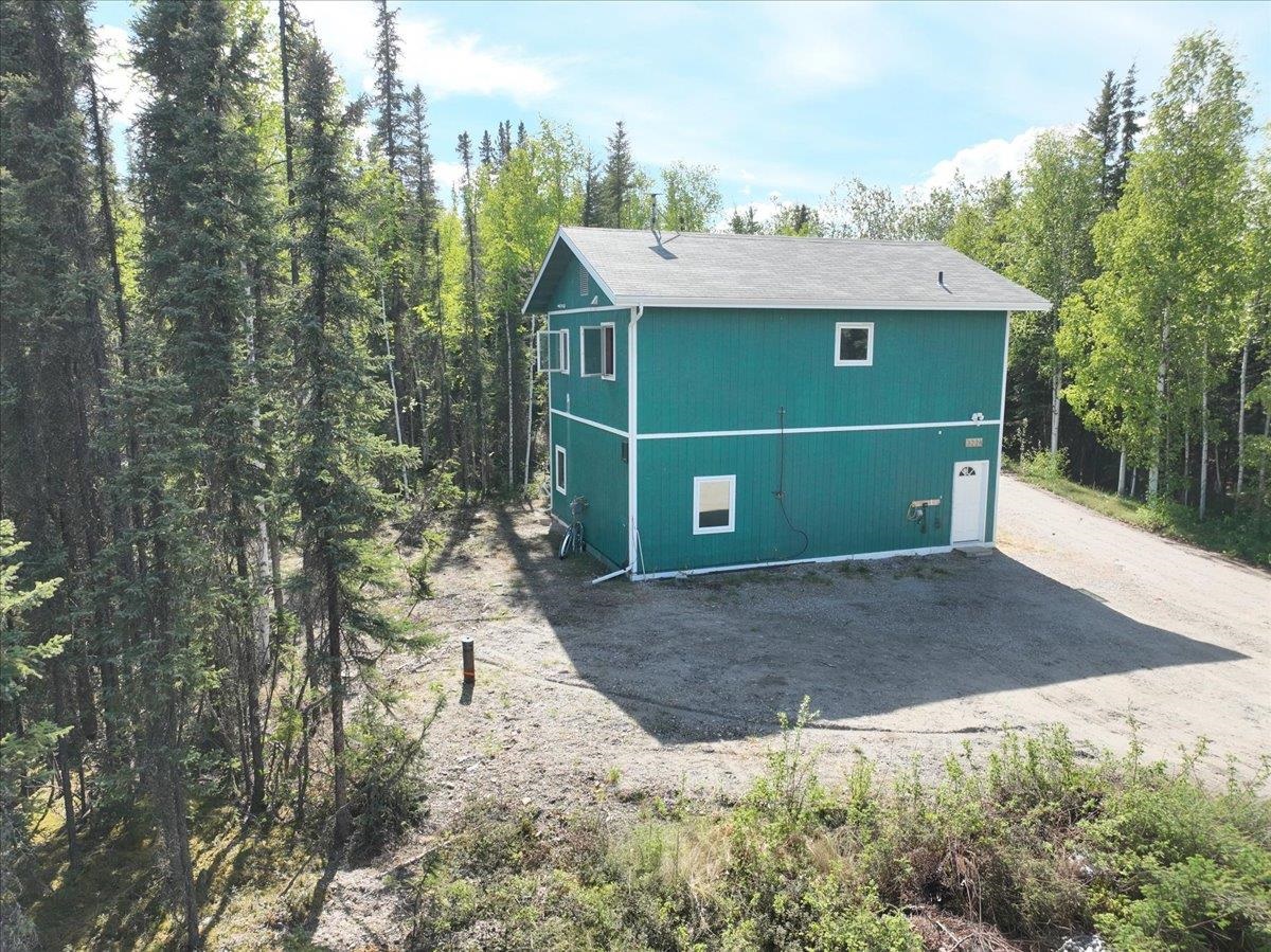 Teal two-story house with white trim, surrounded by trees and a gravel driveway.