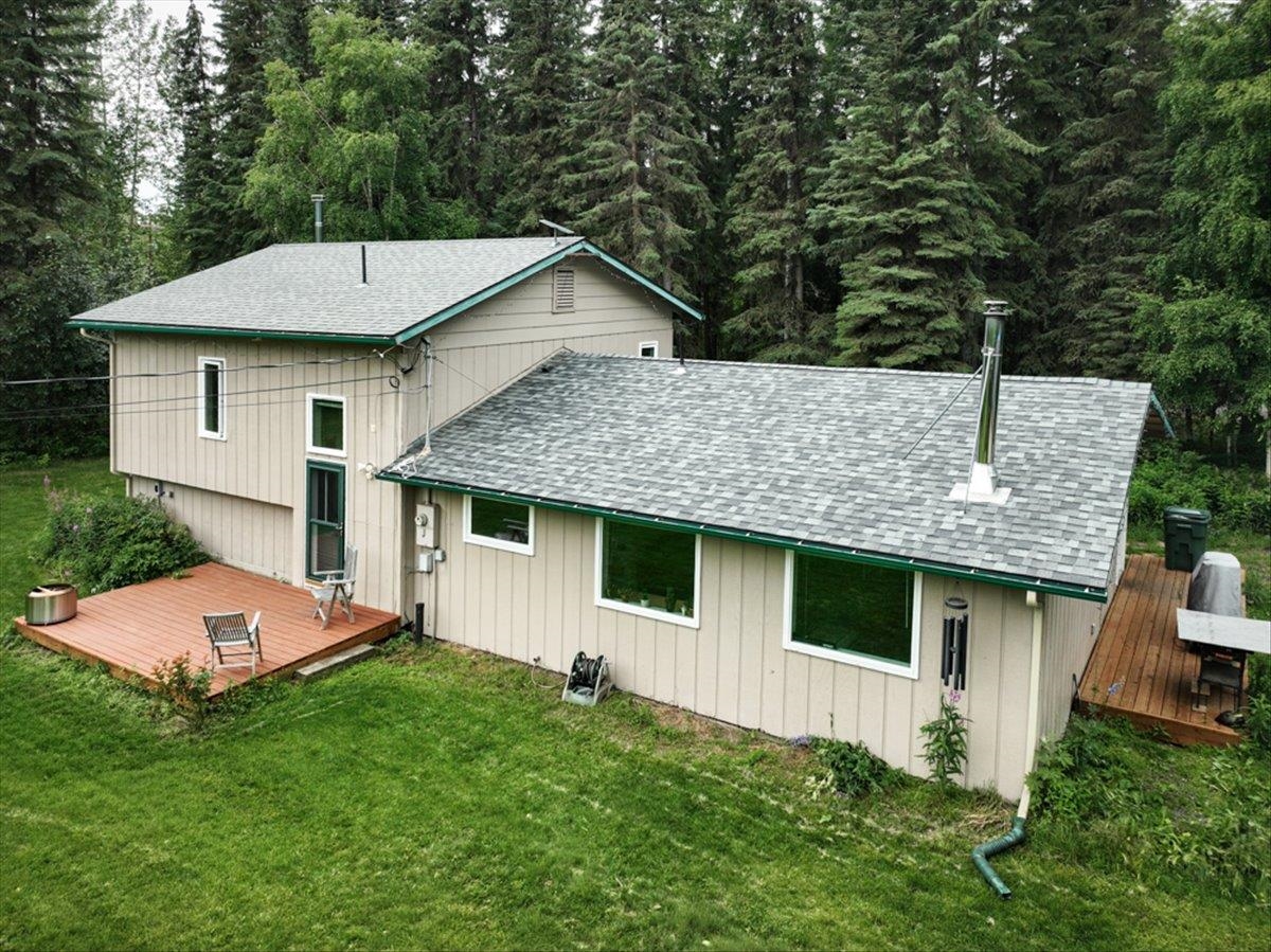 Beige two-story home with wooden decks and a lawn bordered by evergreen forest.