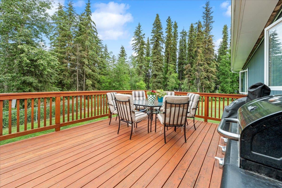 Wooden deck with outdoor dining set and barbecue, overlooking a dense evergreen forest.
