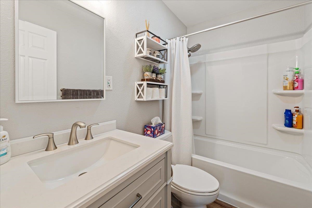 Bathroom with a white vanity, large mirror, toilet, and tub-shower with a curtain.
