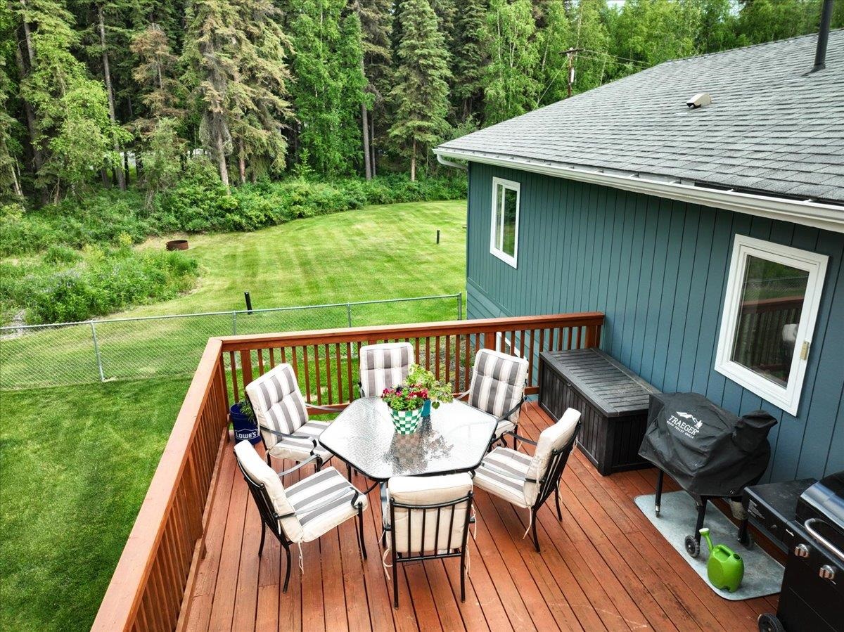 Furnished redwood deck with outdoor dining set overlooking a fenced lawn and wooded yard.