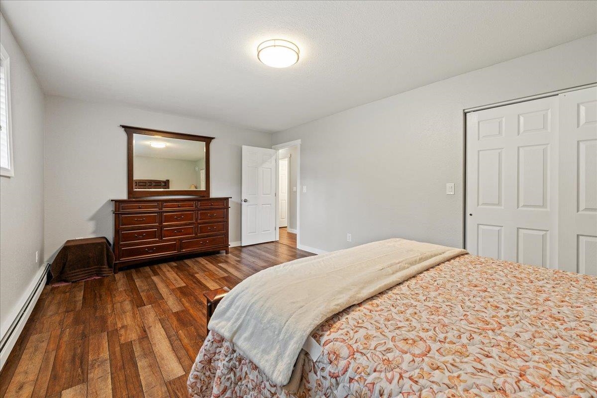 Bedroom with a floral-quilted bed, dark wood dresser and mirror, and hardwood floors.