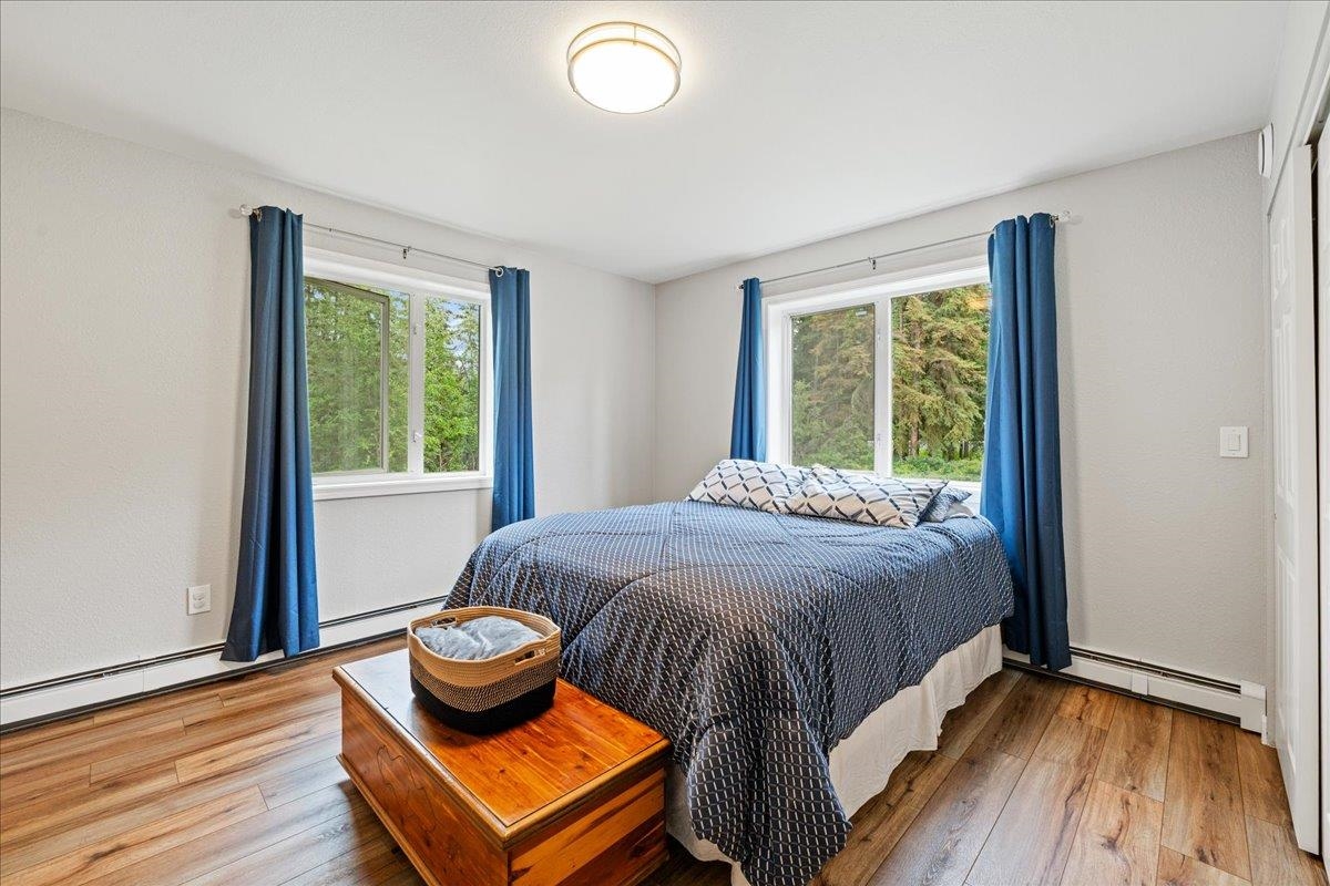 Bedroom with a patterned blue bedspread, blue curtains, and windows overlooking trees.