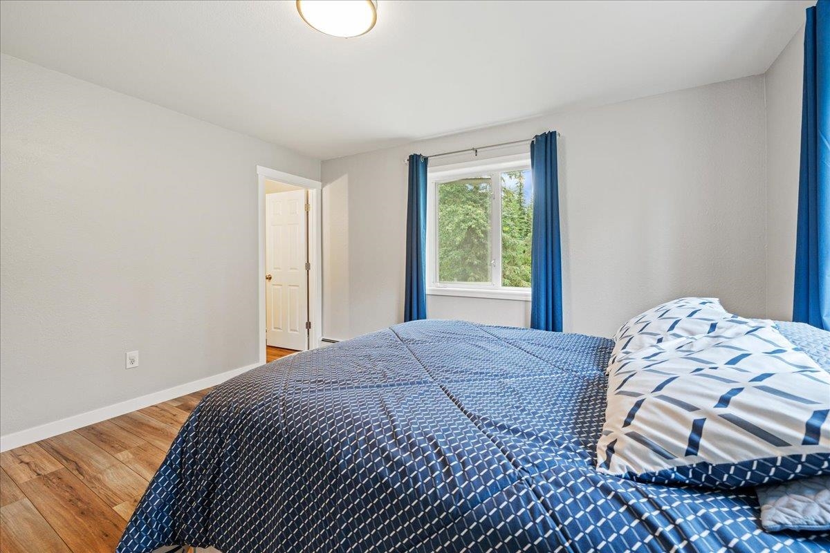 Bedroom with blue patterned bedding, blue curtains, and wood flooring.