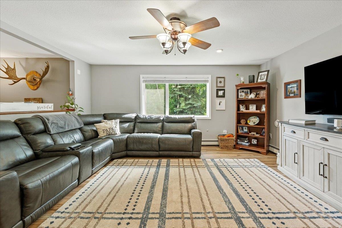 Living room with a leather sectional, patterned rug, ceiling fan, and large window.