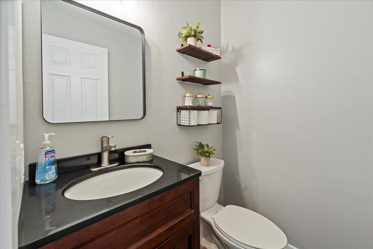 Bathroom with a dark wood vanity, black countertop, oval sink, and floating shelves above the toilet.
