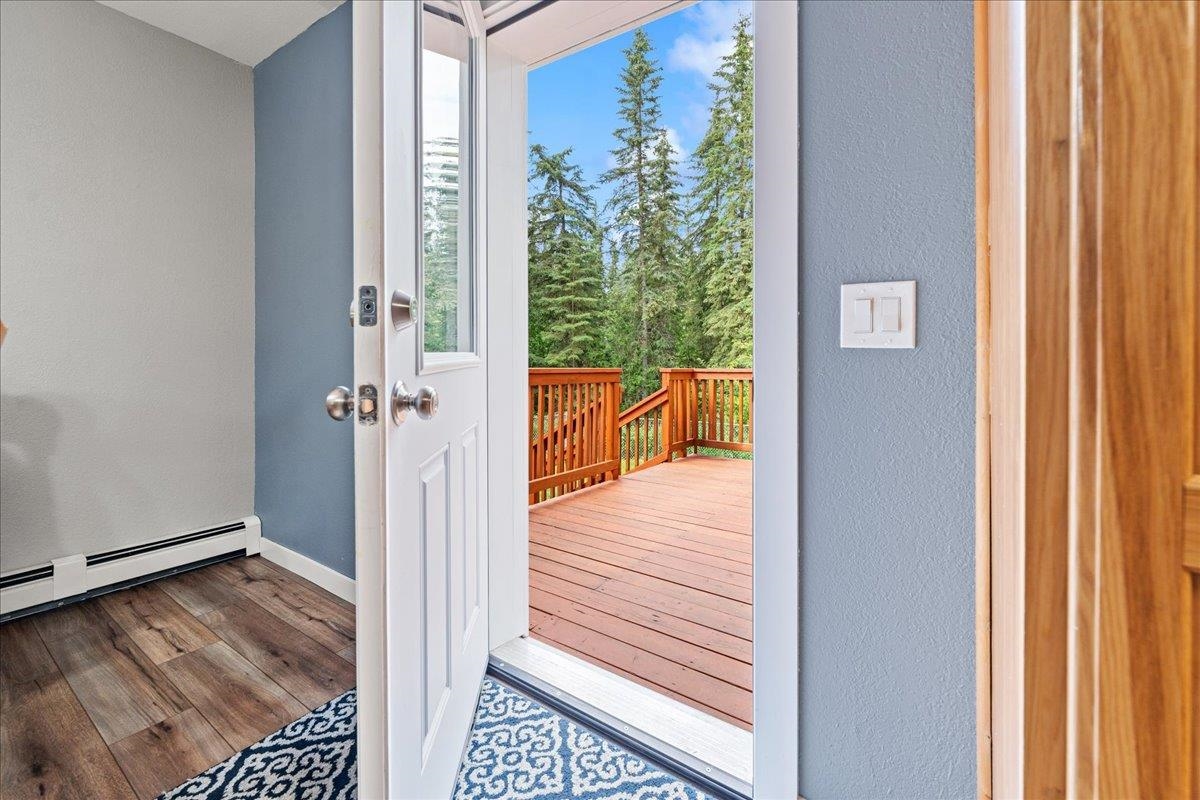 Open entry door onto a wooden deck bordered by evergreen trees.