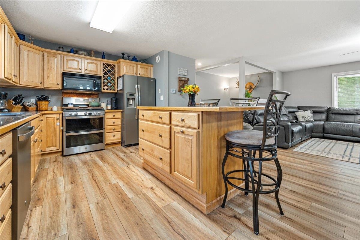 Open-plan kitchen with a wood island, bar seating, stainless steel appliances, and an adjoining living area.