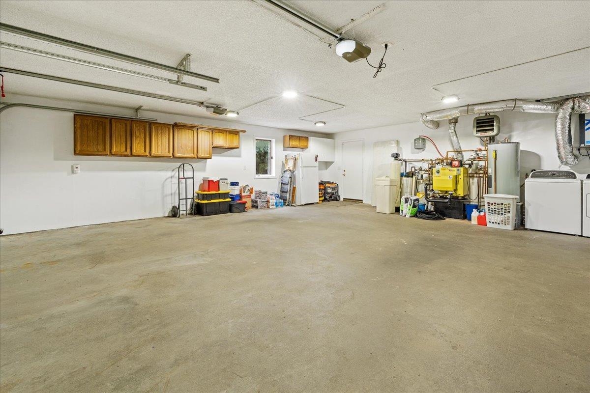 Spacious garage with wooden wall cabinets, laundry appliances, and mechanical equipment along the walls.