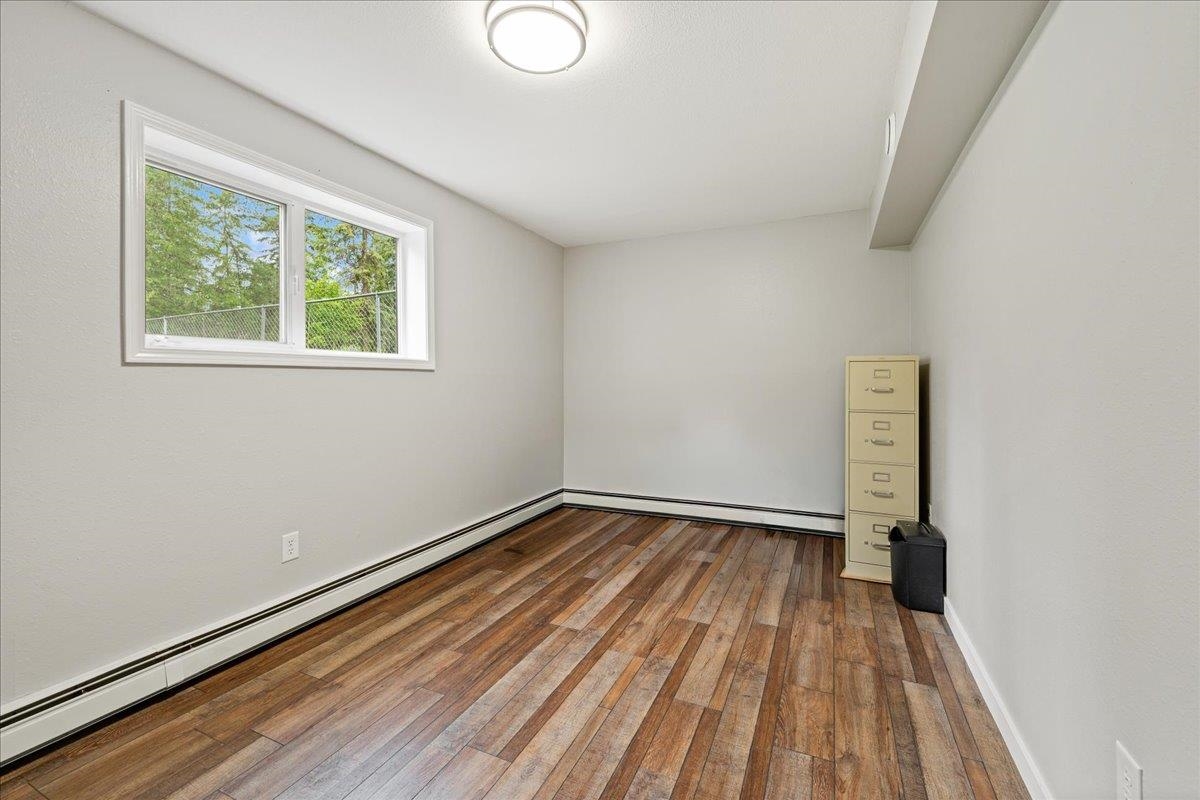 Mostly empty room with wood-look flooring, a wide window, and a filing cabinet in the corner.
