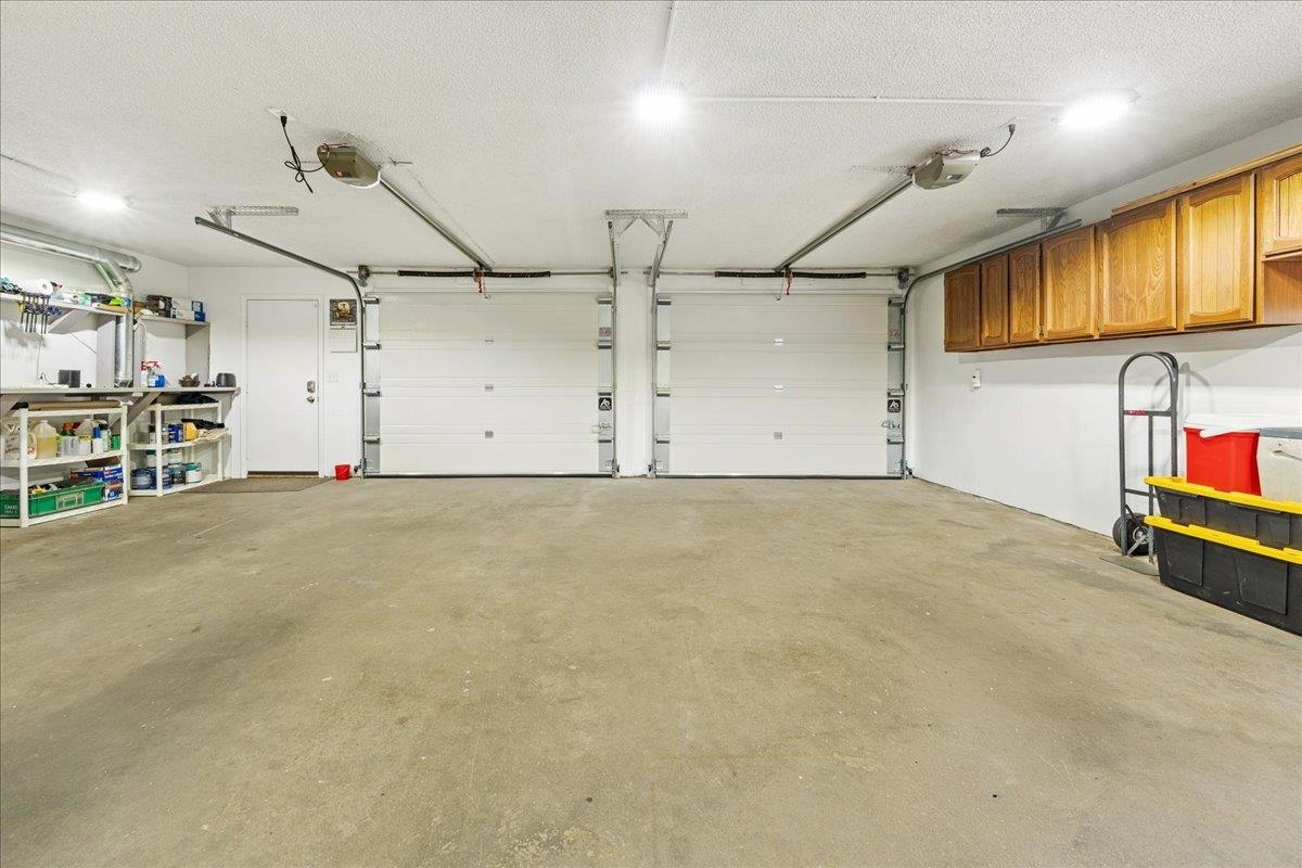 Two-car garage with closed overhead doors, wall shelving, and wooden cabinets.