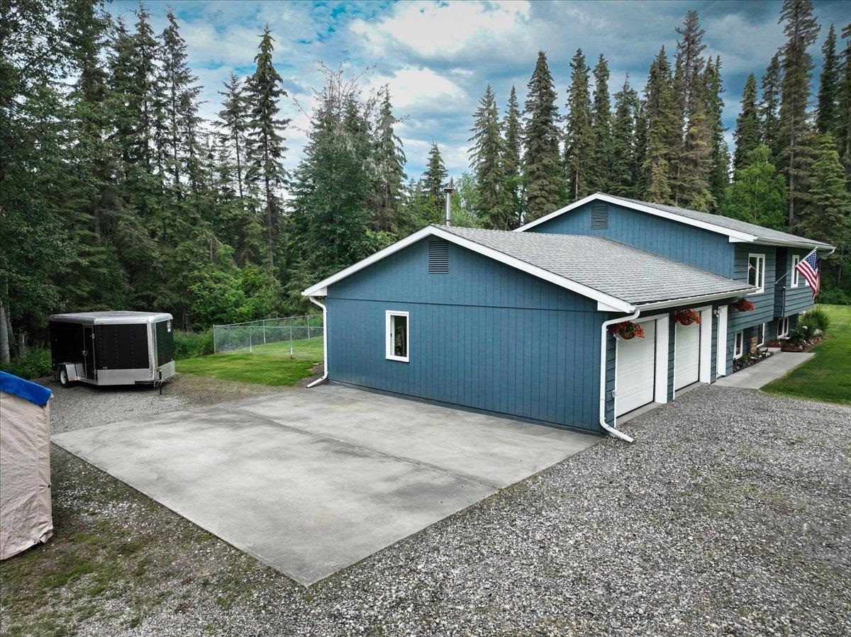 Blue multi-garage home with a broad concrete driveway and wooded surroundings.