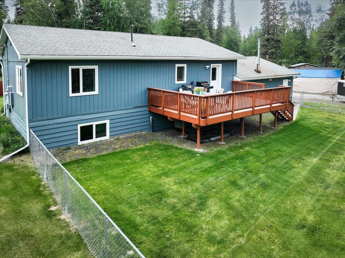 Blue-sided home with a raised wooden deck overlooking a fenced lawn and evergreen trees.