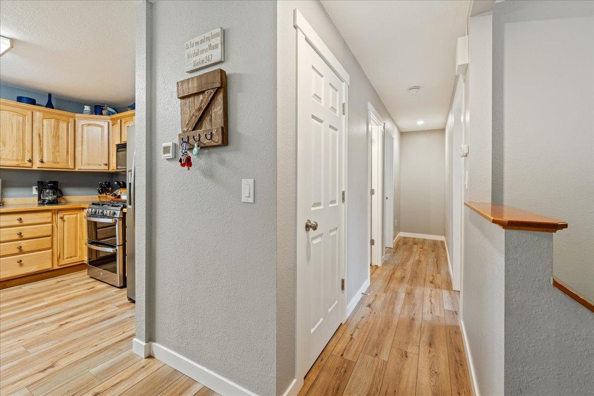 Interior hallway beside a kitchen, with wood-look flooring and light wood cabinets.