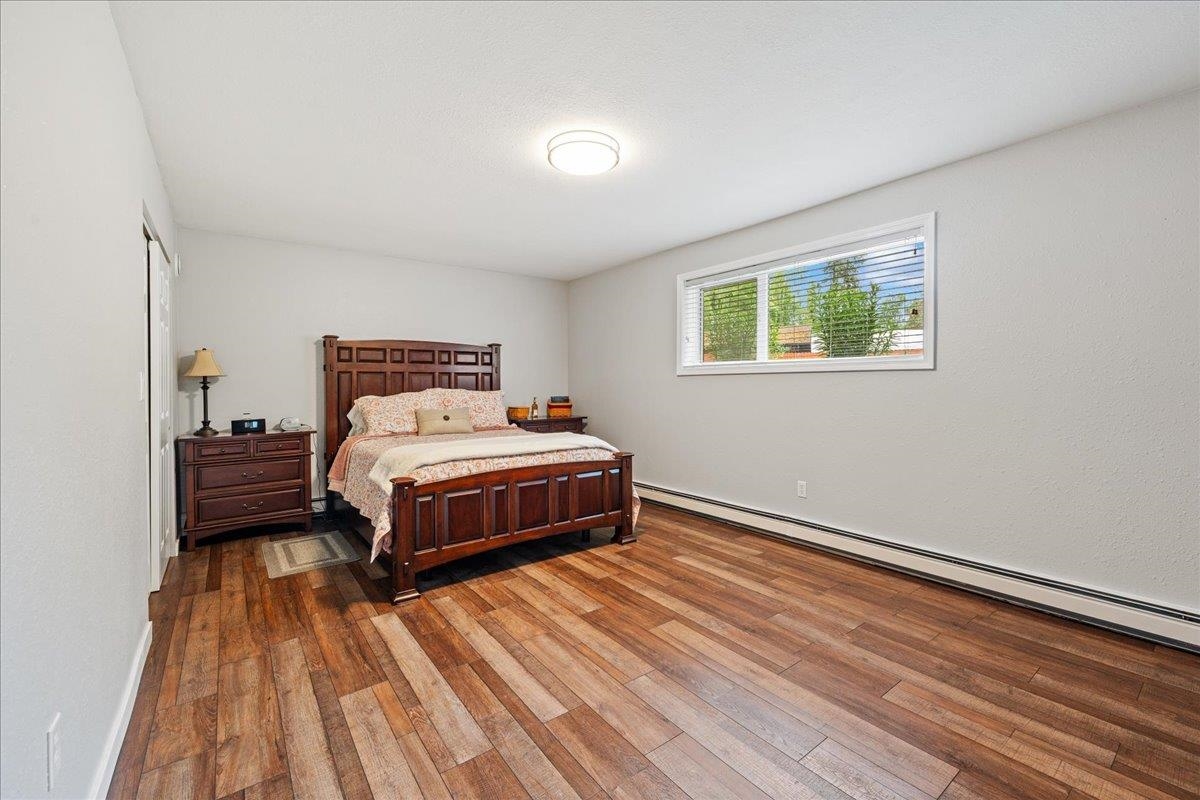 Bedroom with dark wood furniture, patterned bedding, warm-toned plank flooring, and a wide window.