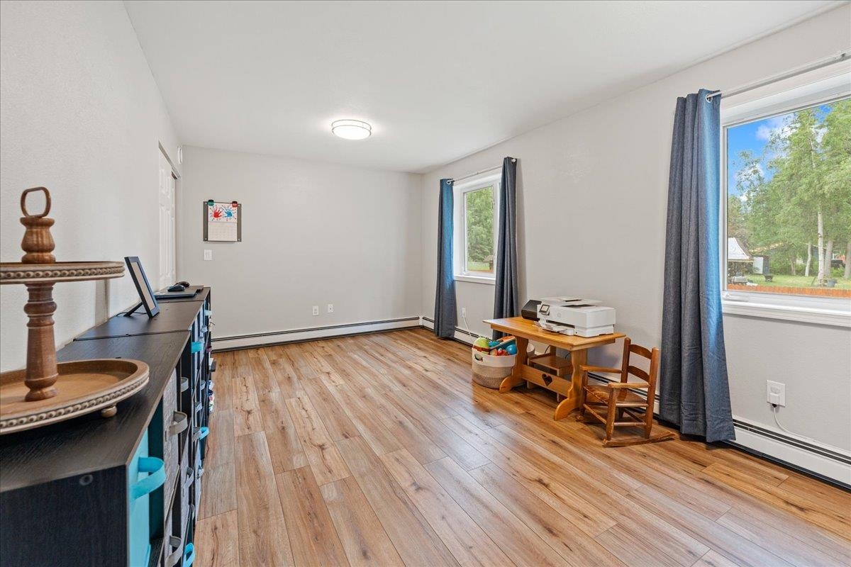 Furnished room with wood-look flooring, two curtained windows, and a desk with a printer.