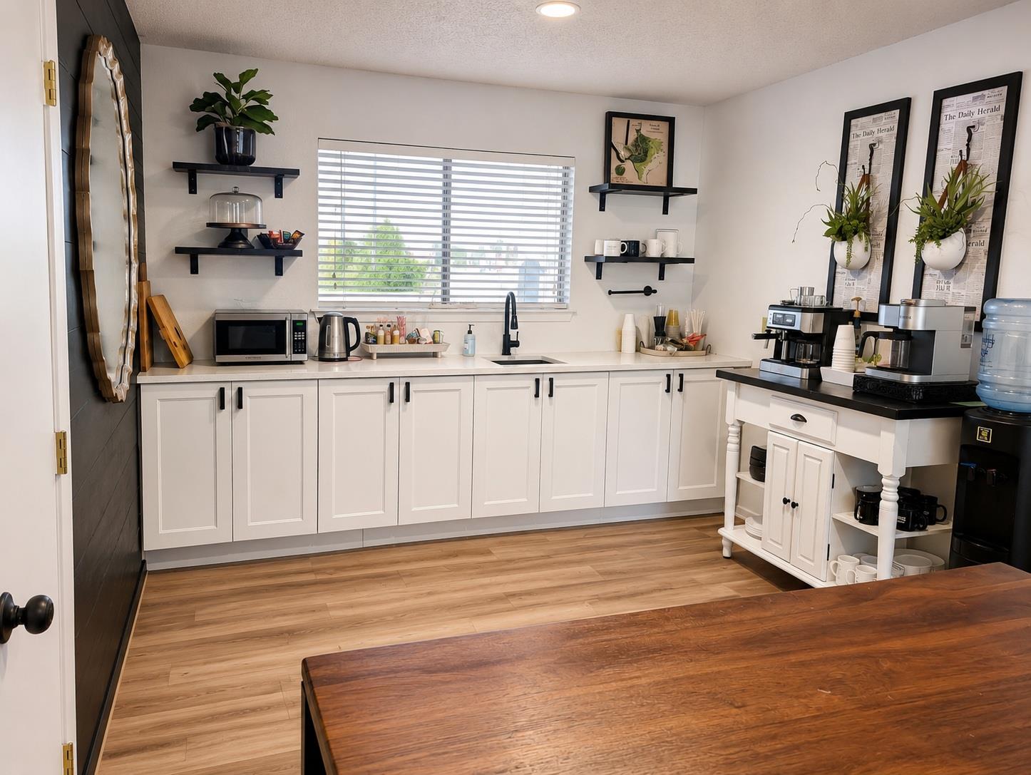 Kitchen with white cabinets, a wide window, and a coffee station with multiple machines.