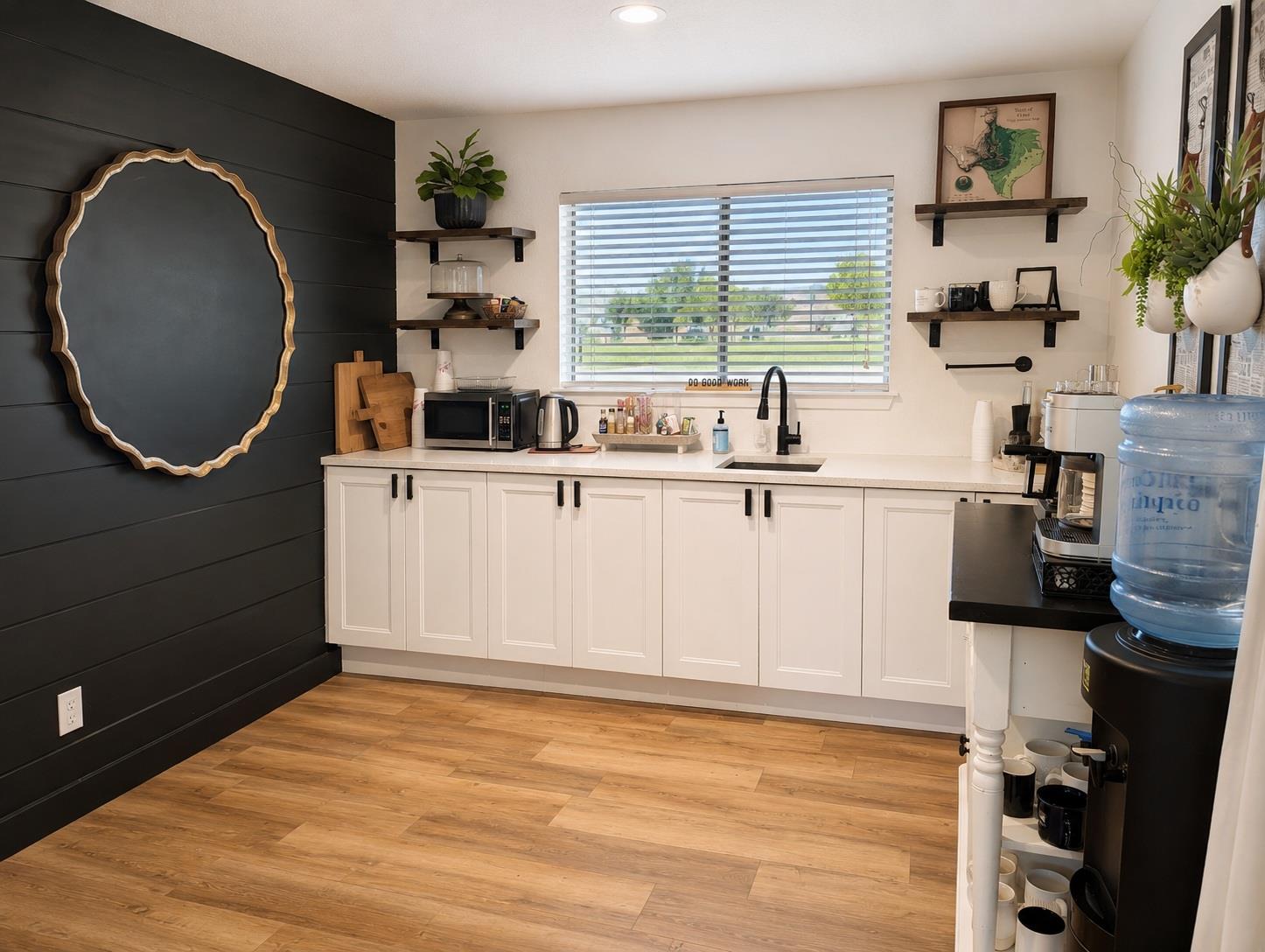 Kitchenette with white cabinets, black accent wall, window, and coffee station.
