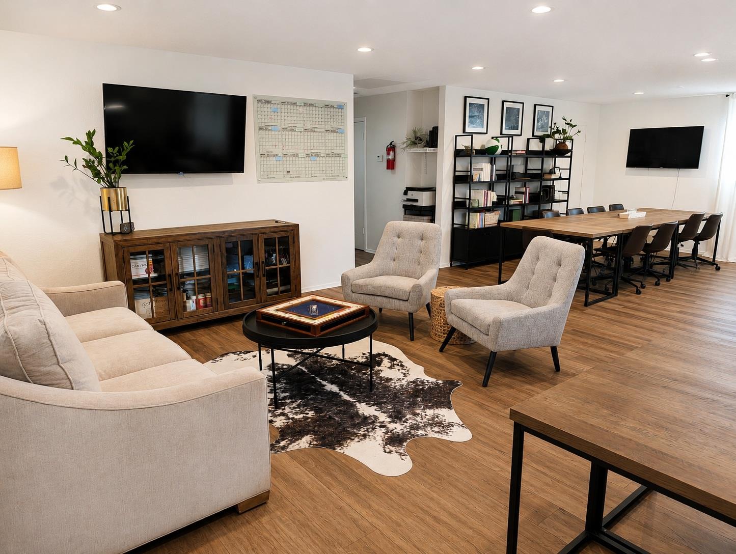 Open-plan living and meeting area with beige seating, wood-look floors, and a long conference table.