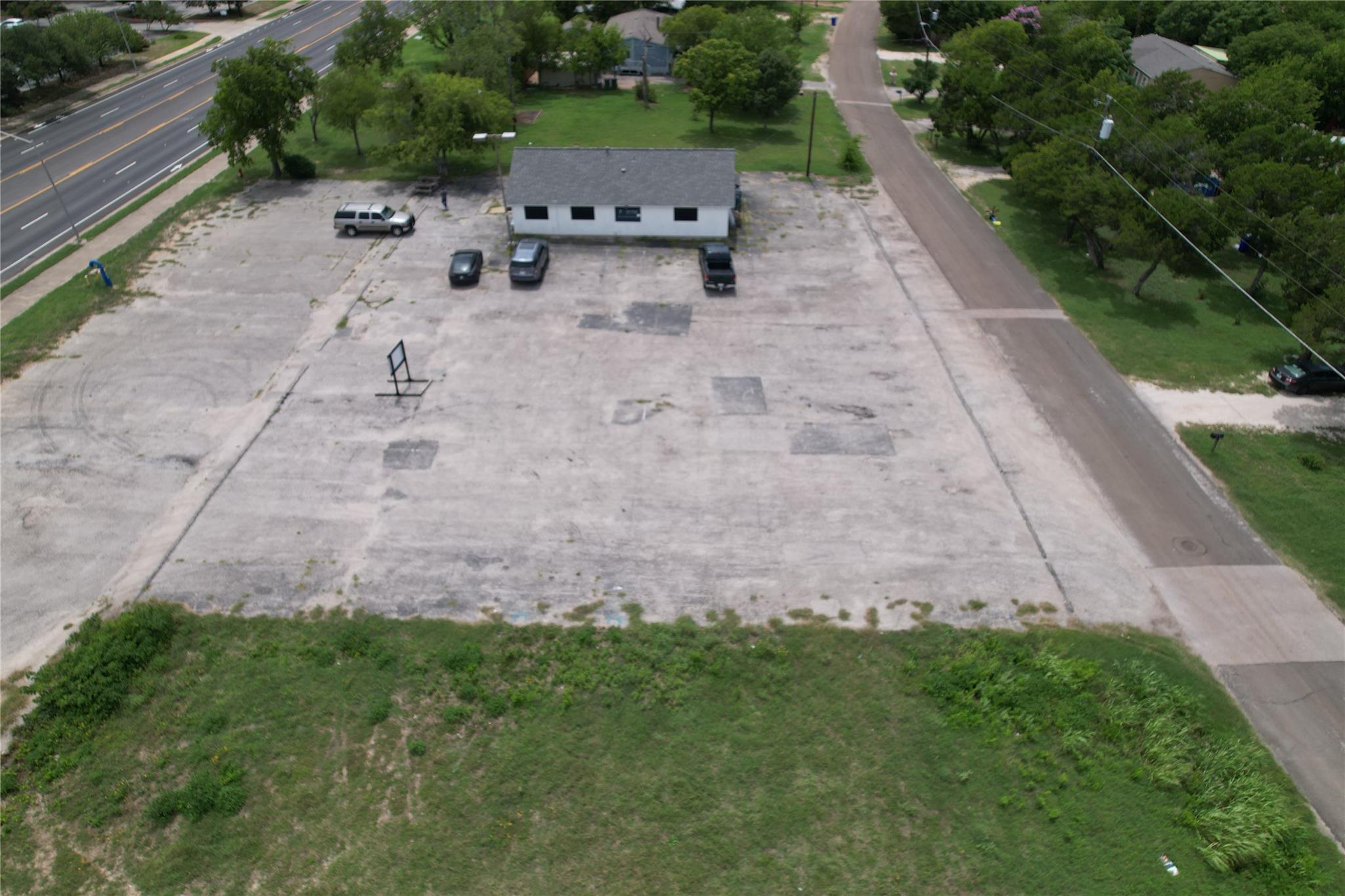Aerial view of a one-story commercial building and expansive paved lot beside a busy road.
