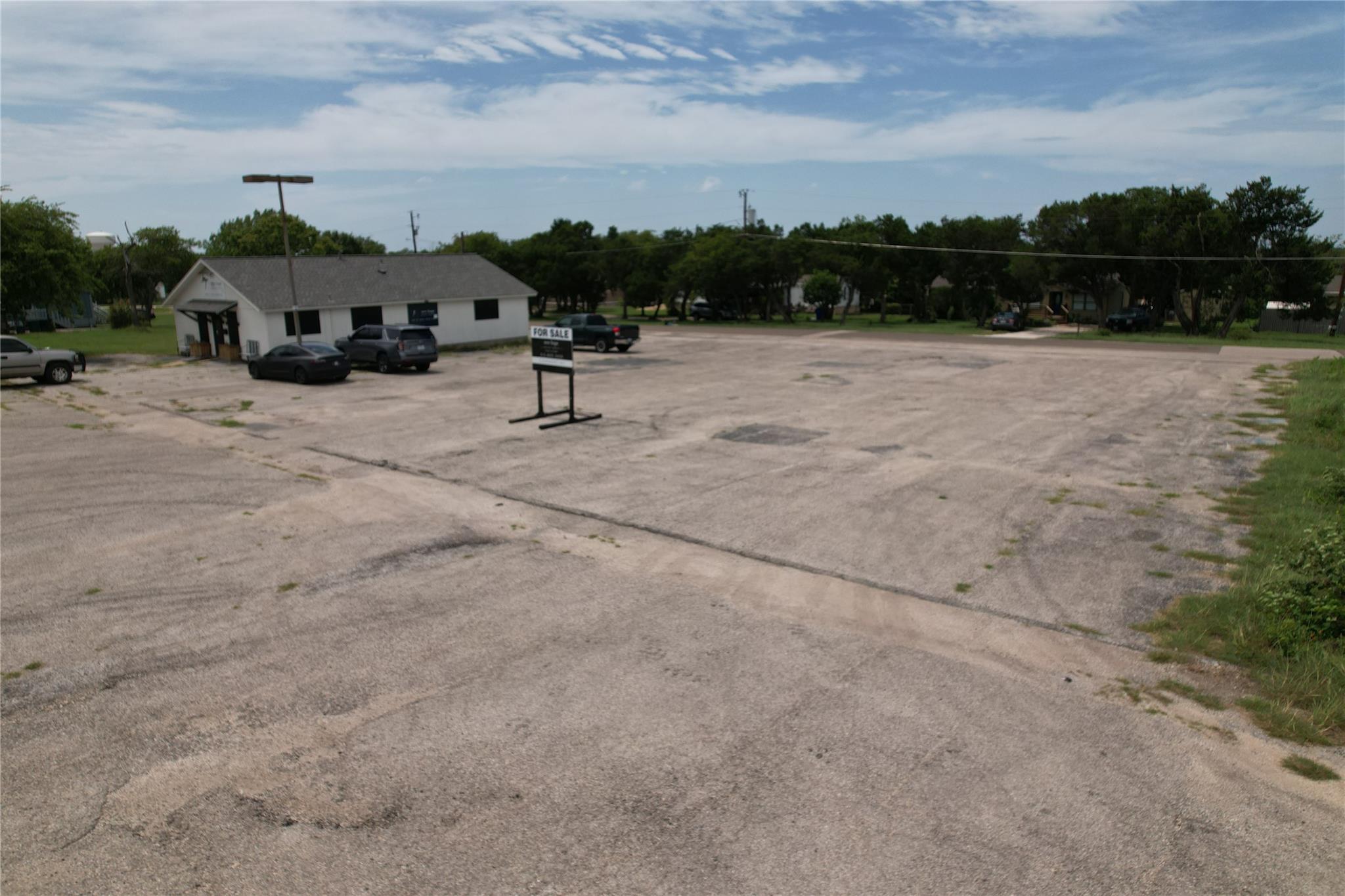 Small white commercial building beside a large asphalt parking lot with a FOR SALE sign.