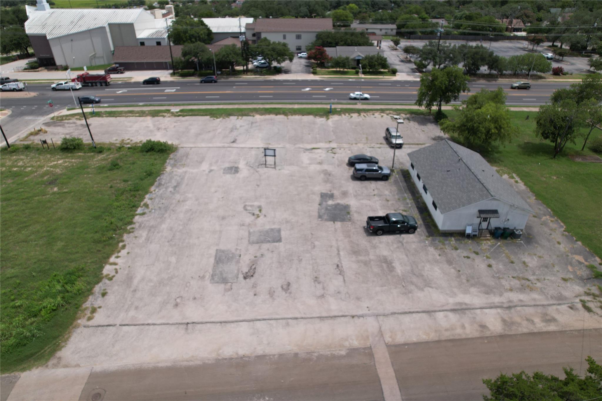 Aerial view of a paved commercial lot with a small building beside a busy road.