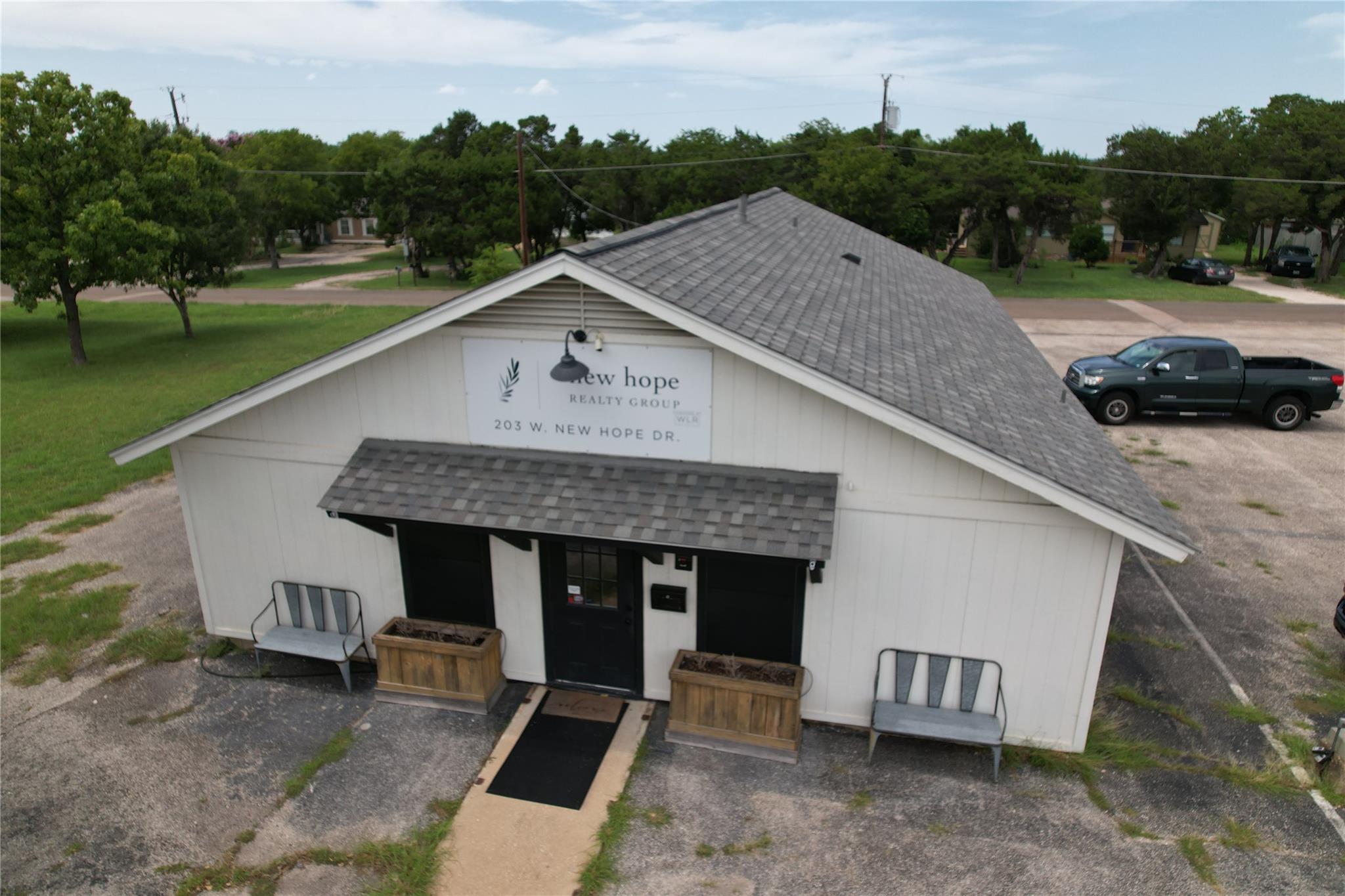White New Hope Realty Group office with a gray shingle roof, black entry, benches, and wooden planters.