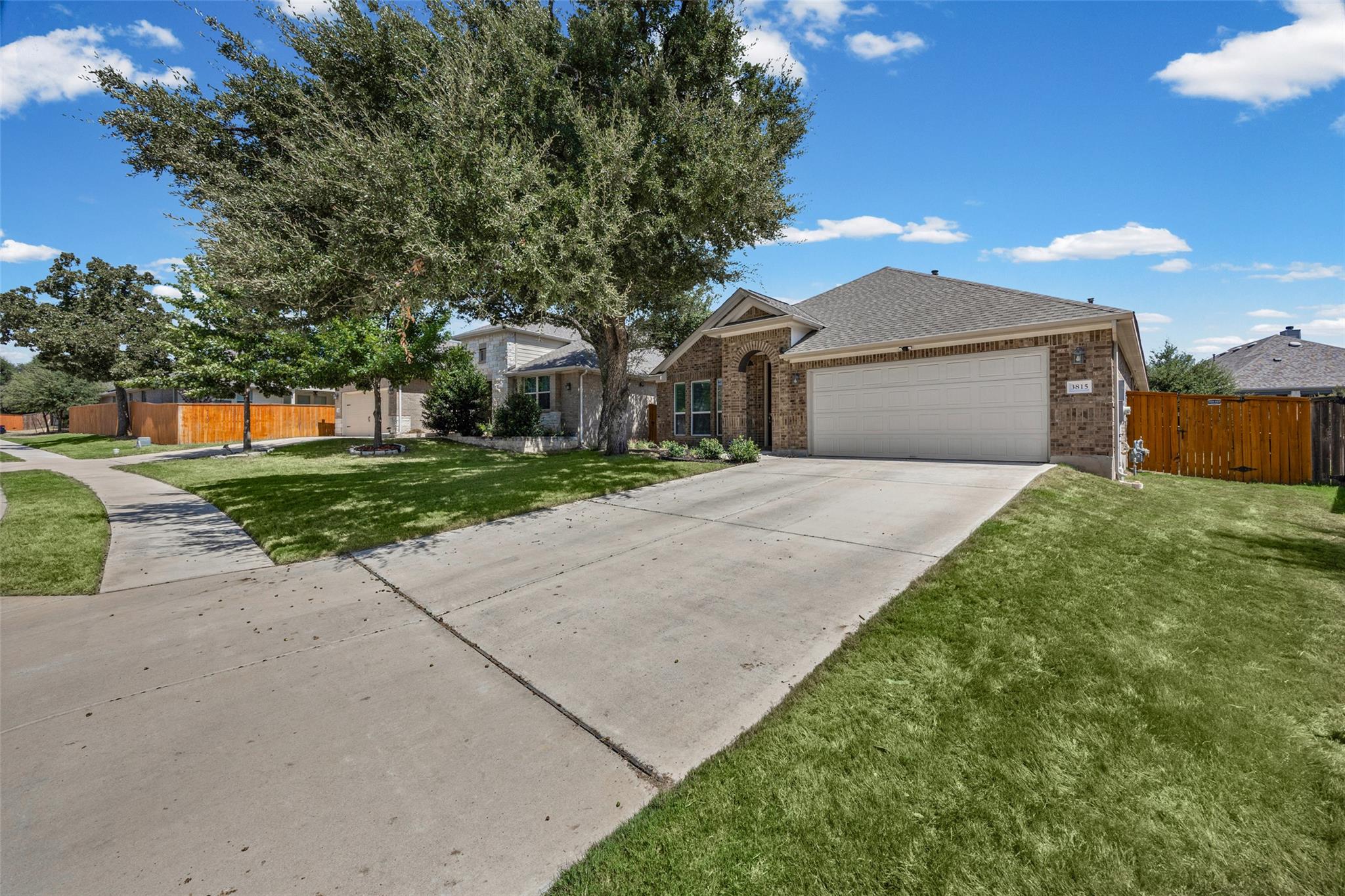Single-story brick home with a two-car garage, broad driveway, and large shade tree.