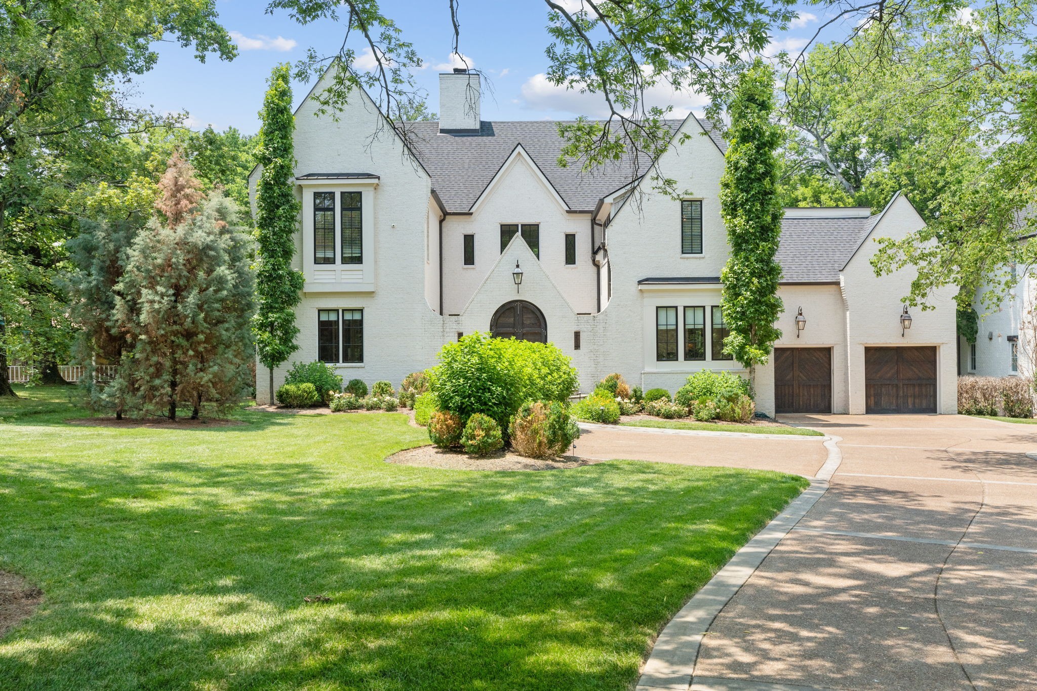 White brick home with a steep gabled roof, arched entry, and two wood garage doors.