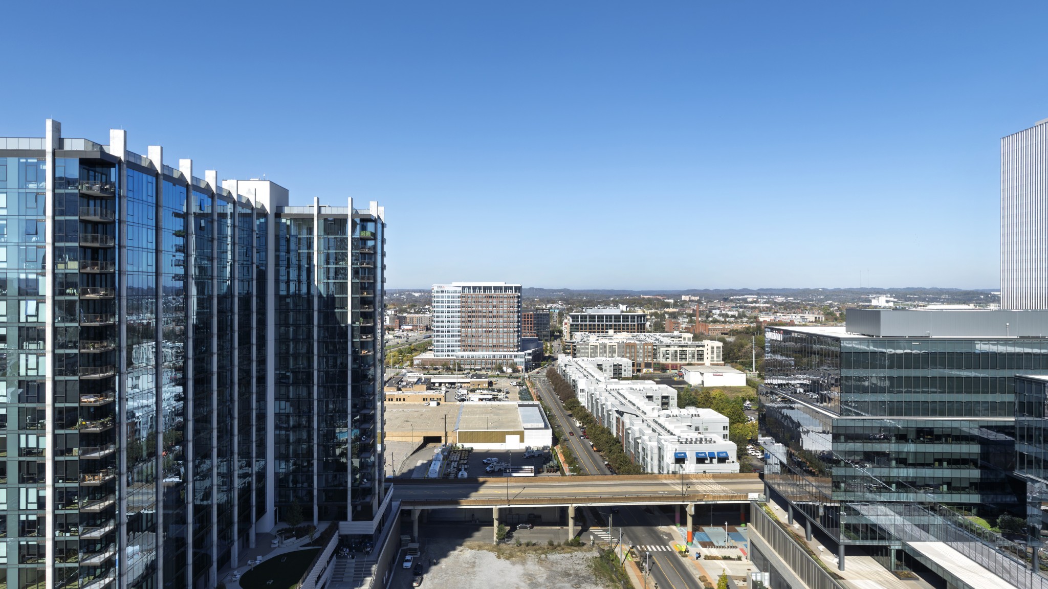 Panoramic city view between glass towers, with downtown buildings and distant hills.