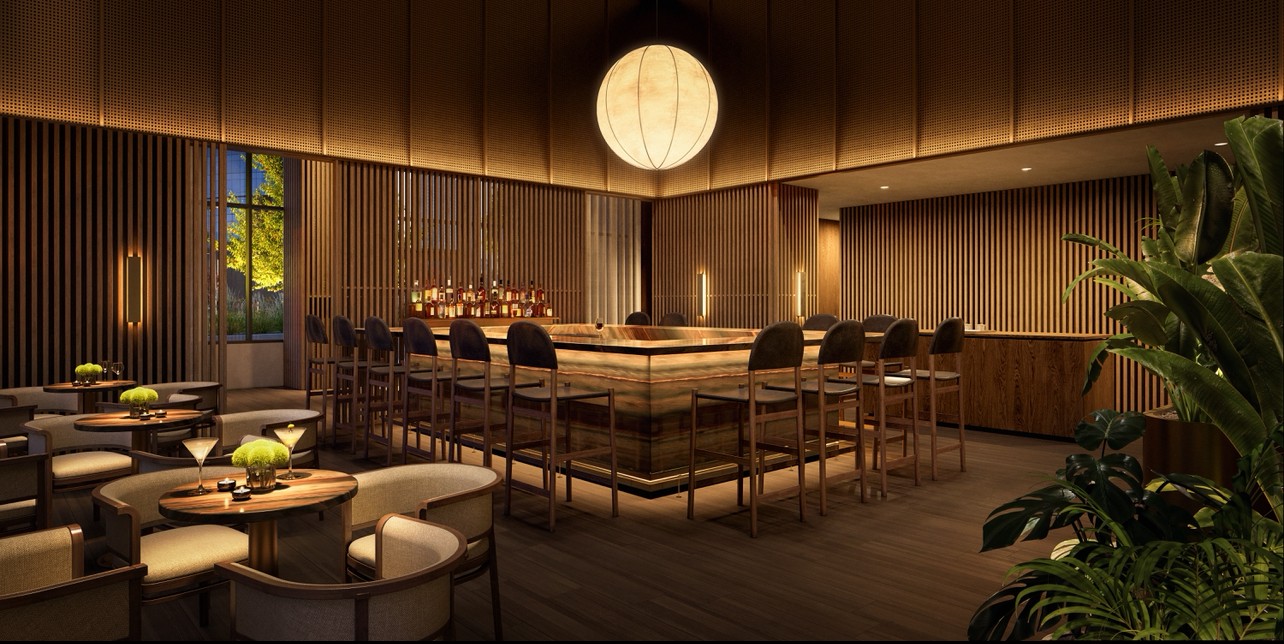 Communal bar lounge with a central bar, wood-slat walls, upholstered seating, and indoor plants.