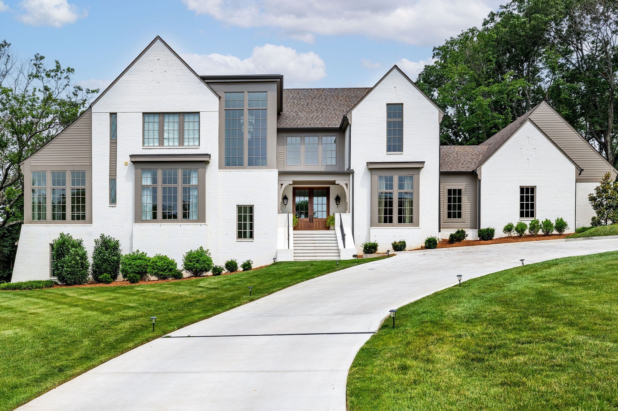Large white brick home with multiple gables, a curved driveway, and manicured lawn.
