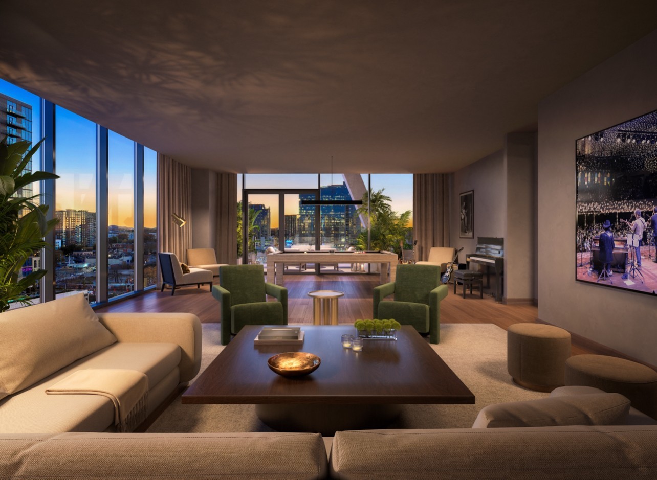 High-rise living room with floor-to-ceiling windows, green armchairs, and a sunset view of the city skyline.