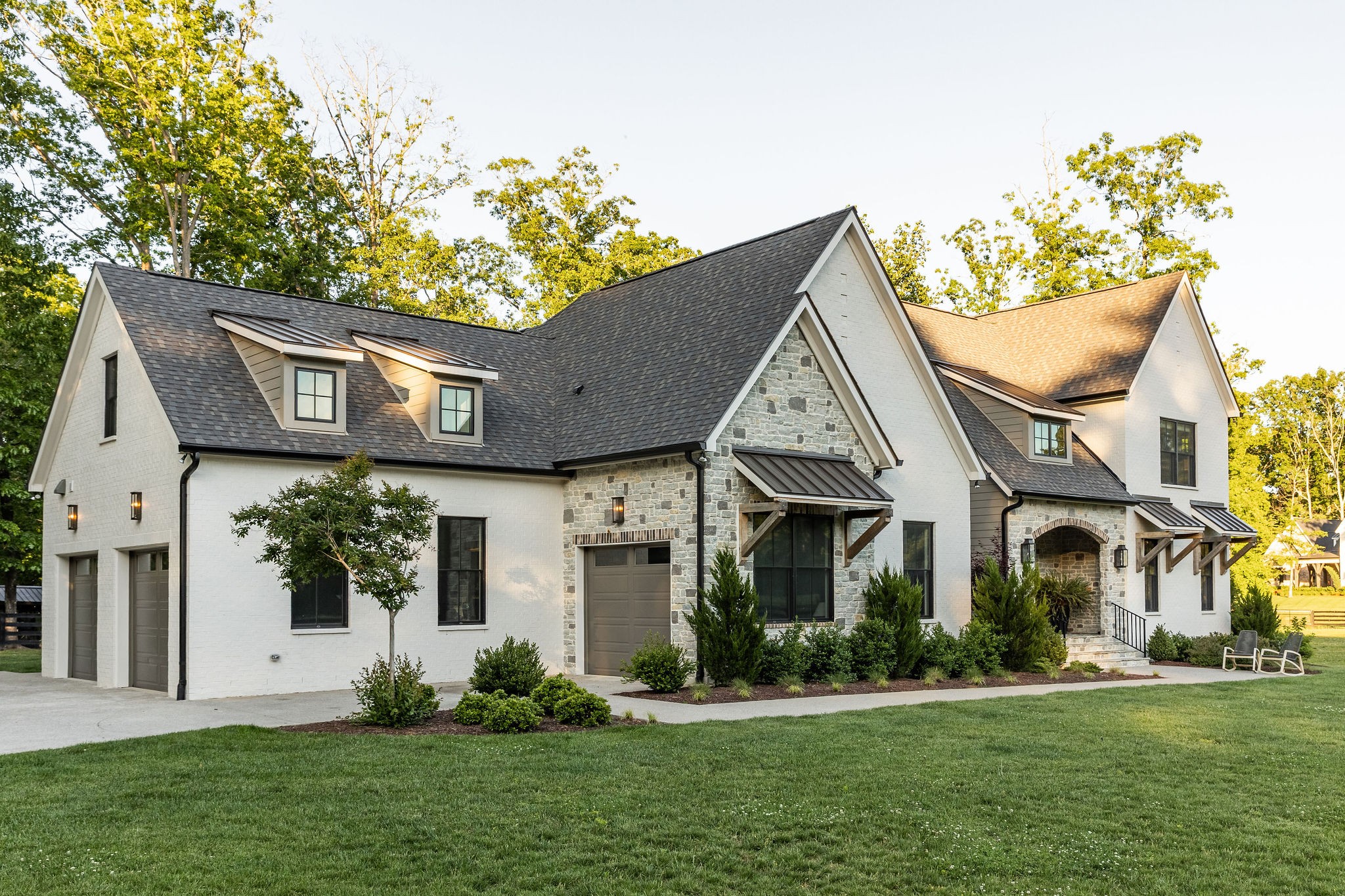 White-brick home with stone accents, steep gabled roofs, dormer windows, and a landscaped lawn.