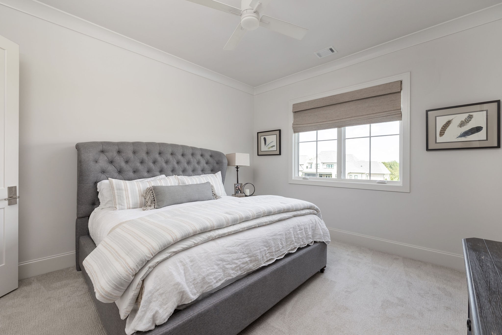 Bedroom with a gray tufted bed and white striped bedding beside a window with a taupe shade.