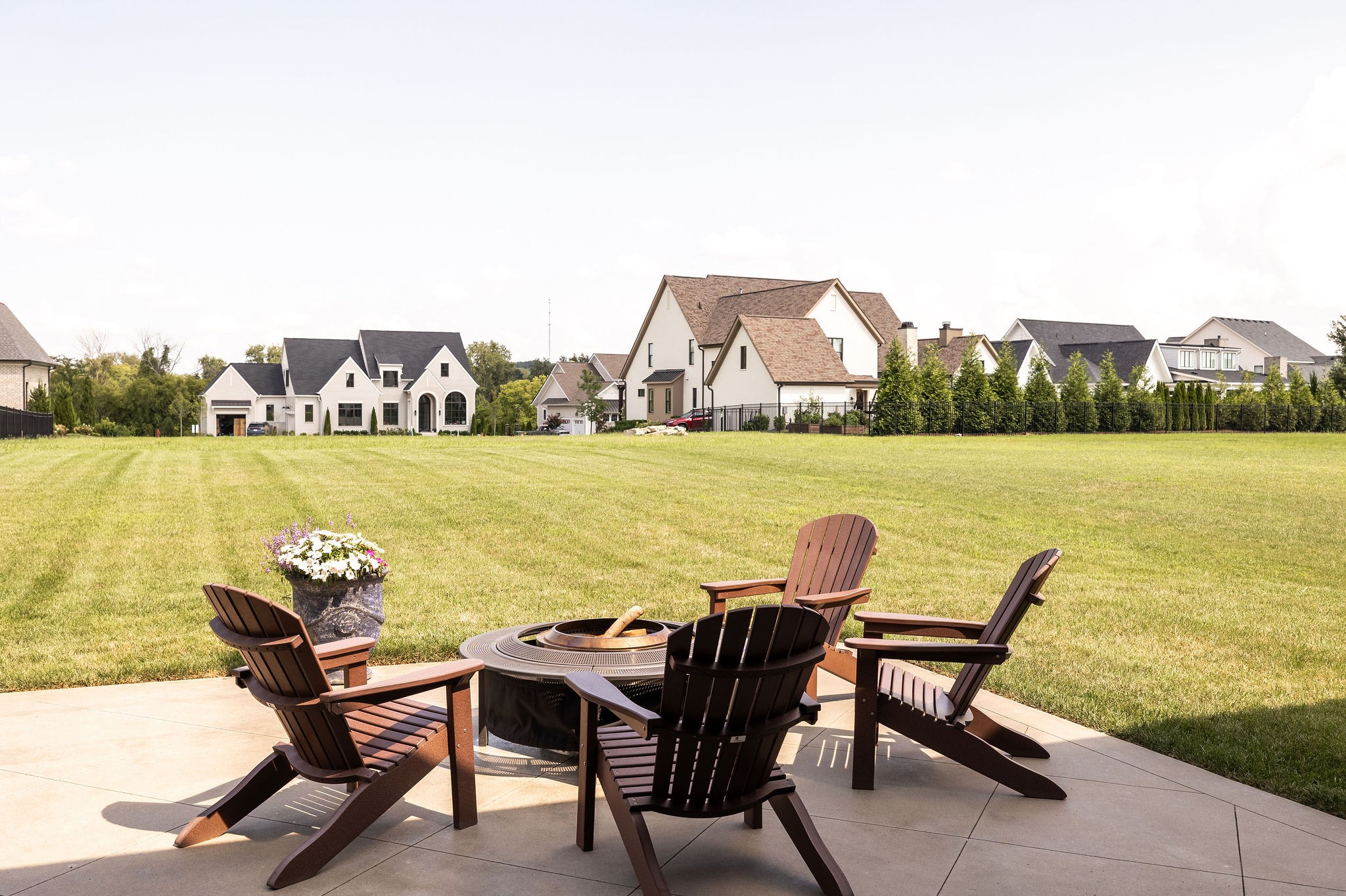Patio with Adirondack chairs around a fire pit, overlooking a broad lawn and neighboring homes.