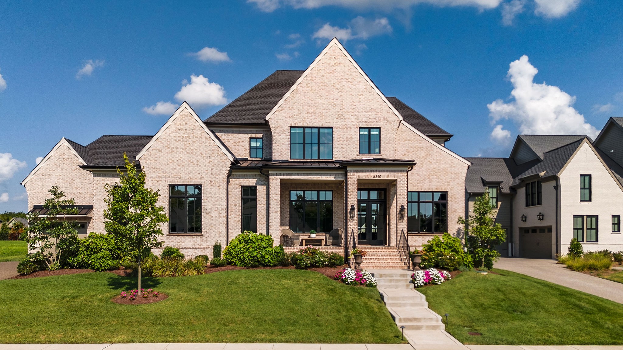 Large brick home with gabled roof, landscaped lawn, and a walkway leading to the covered entrance.