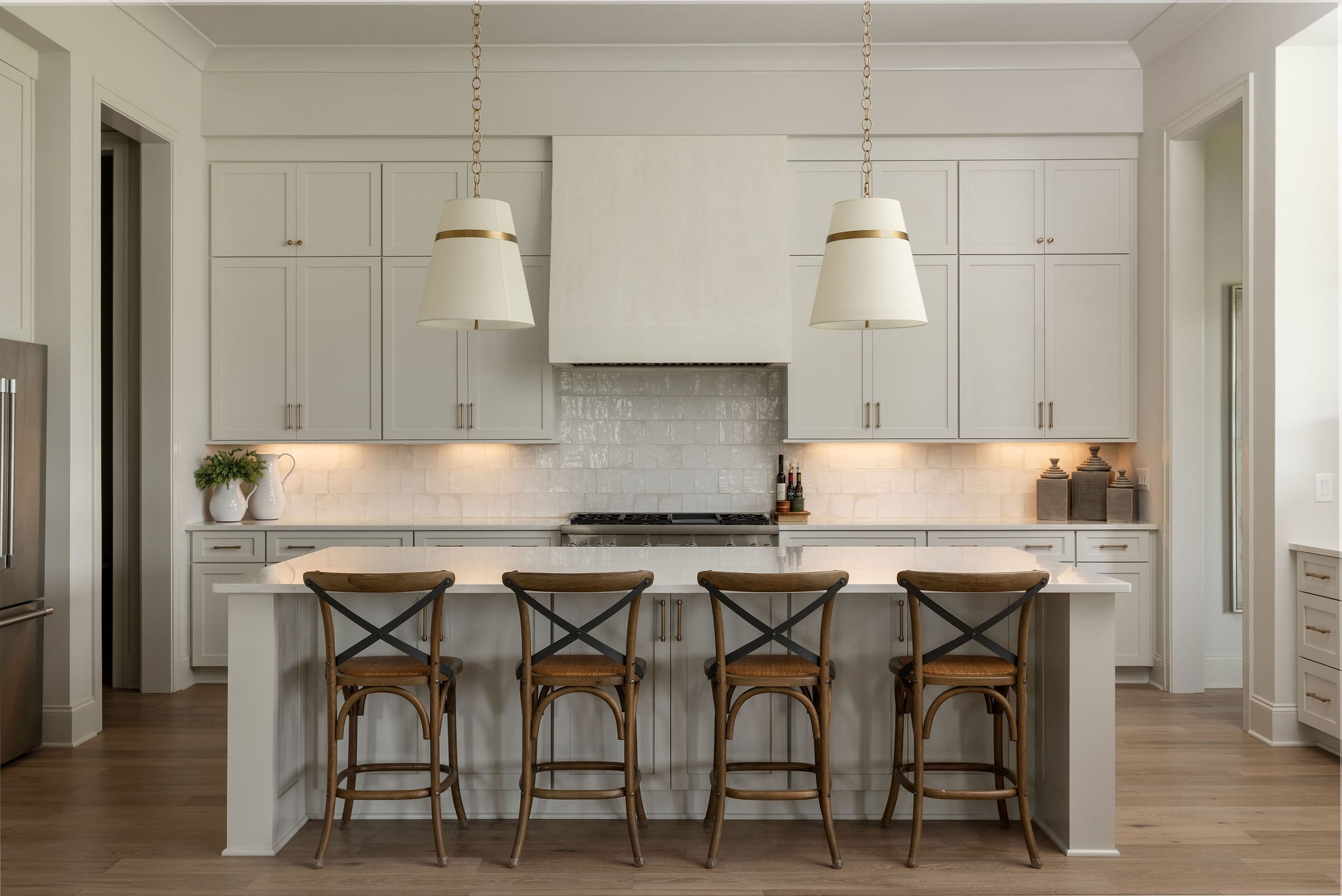 Kitchen with a large white island, four wooden stools, light gray cabinets, and a gas range.