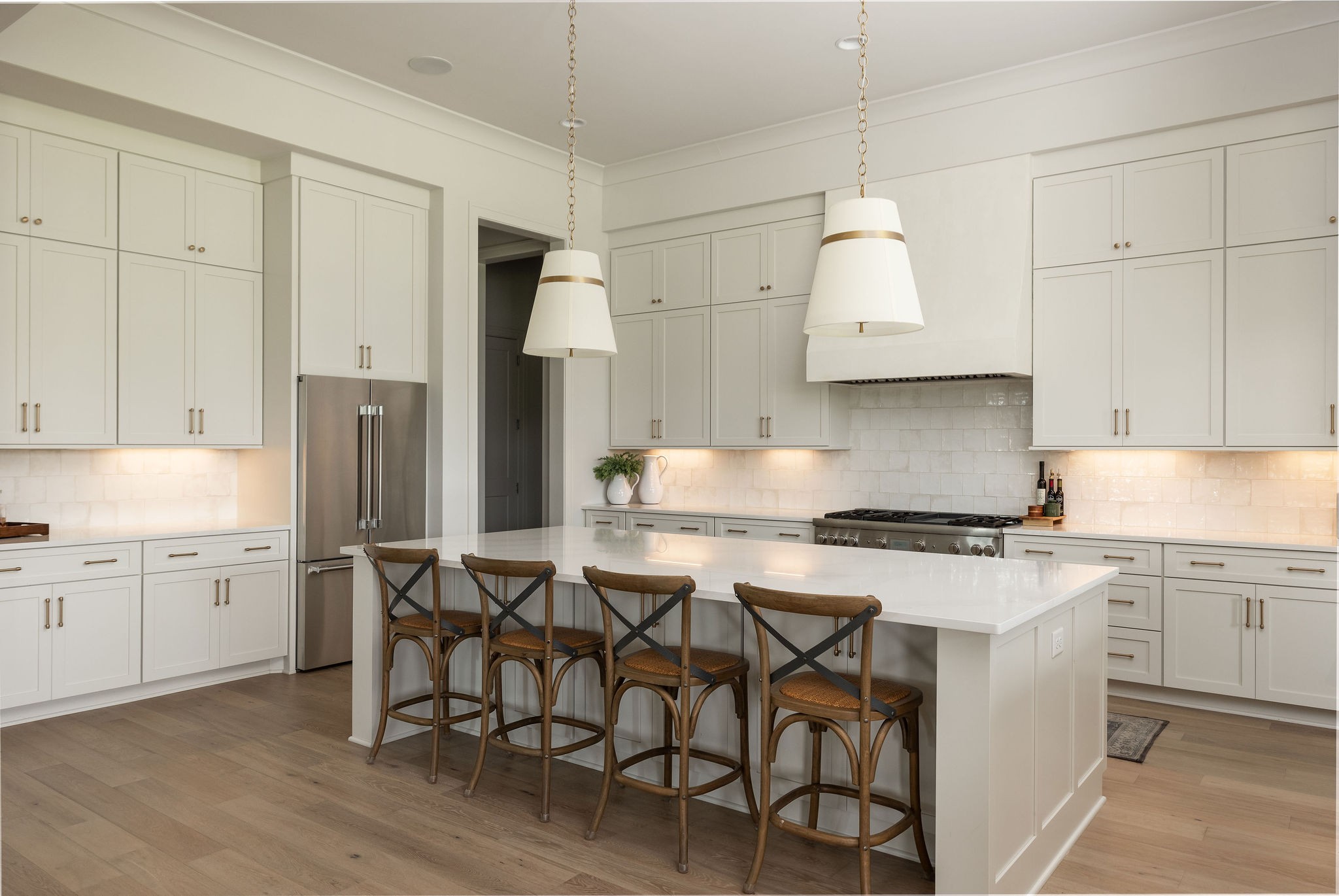 Bright white kitchen with a large island, four wooden stools, and stainless steel appliances.