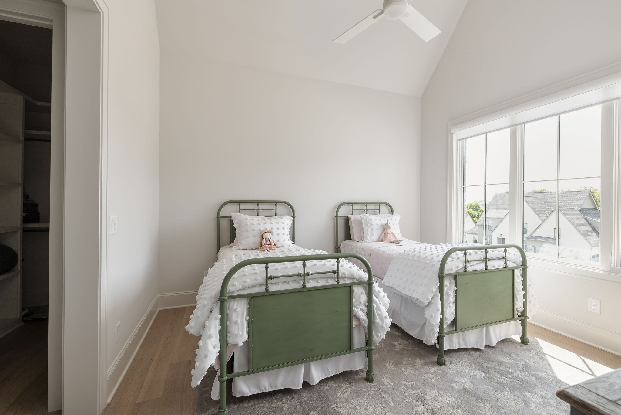 Bedroom with two green metal twin beds beside a large window overlooking neighboring homes.