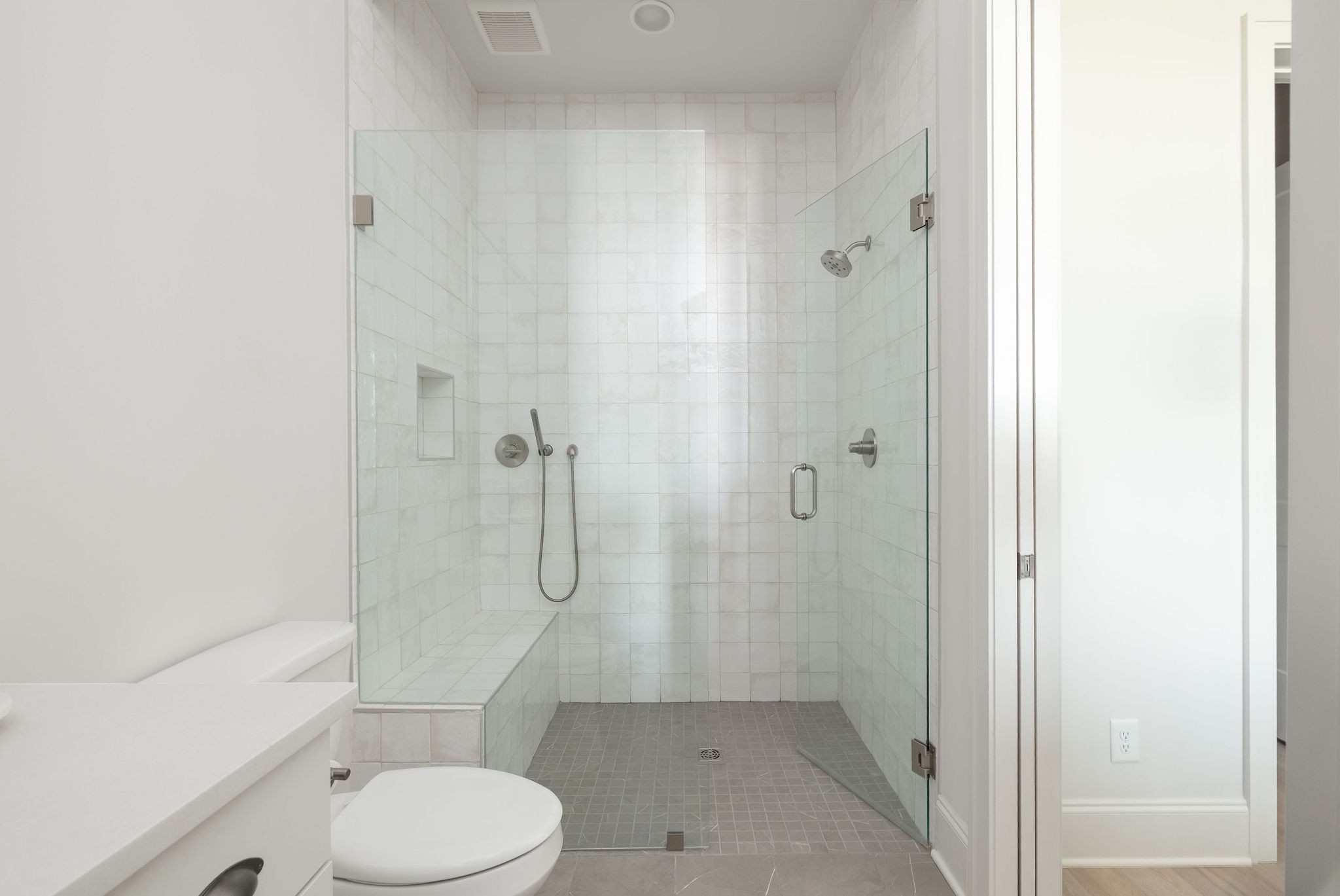 Bathroom with a spacious glass-enclosed tiled shower and built-in bench.
