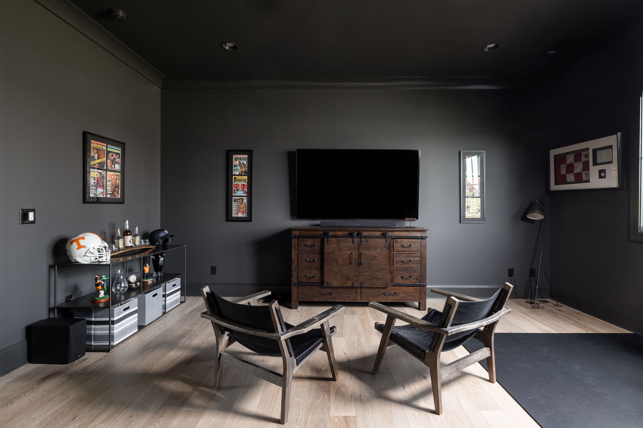 Media room with a large television, two lounge chairs, and framed boxing memorabilia.