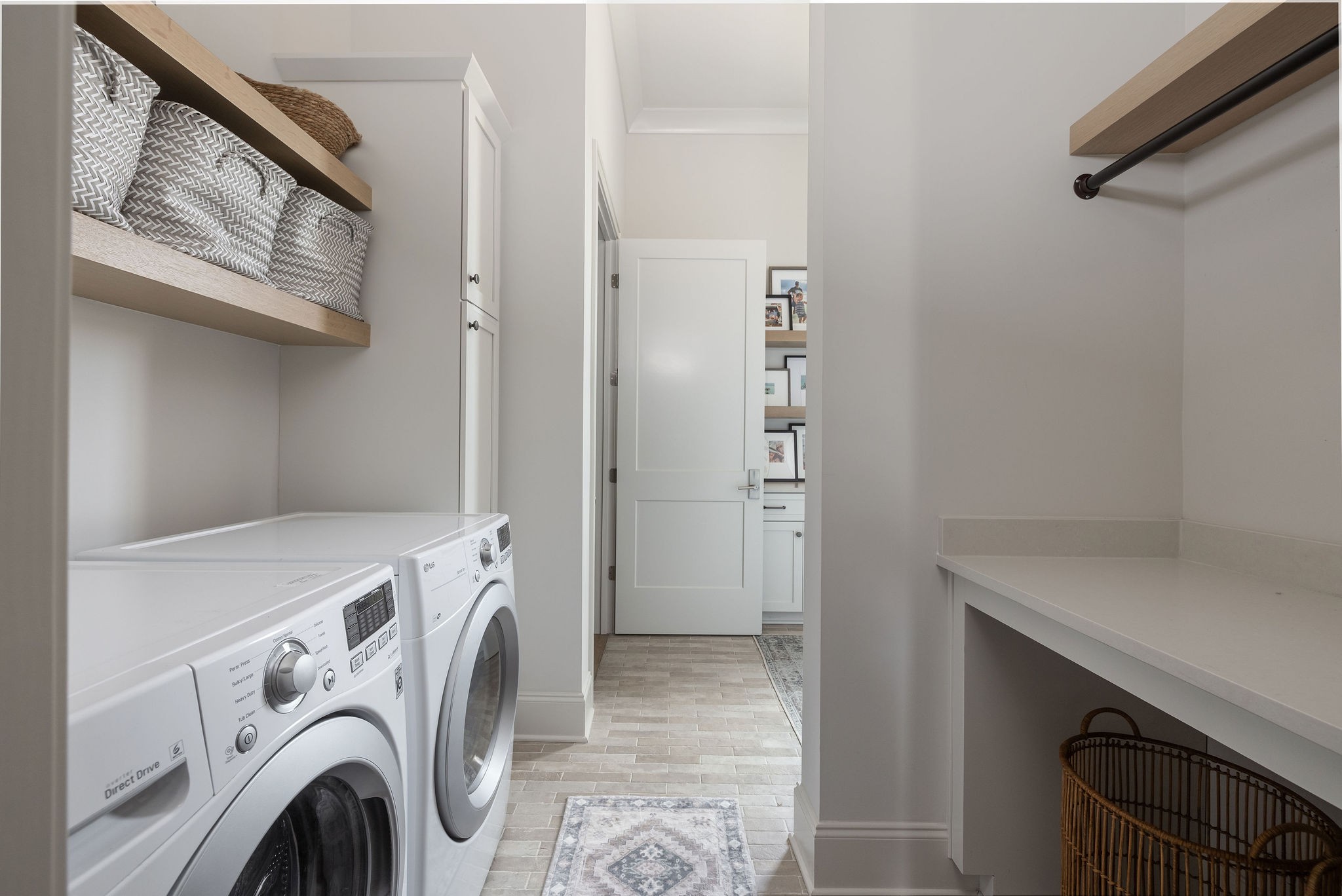 Laundry room with front-loading washer and dryer, open linen shelves, and a long folding counter.