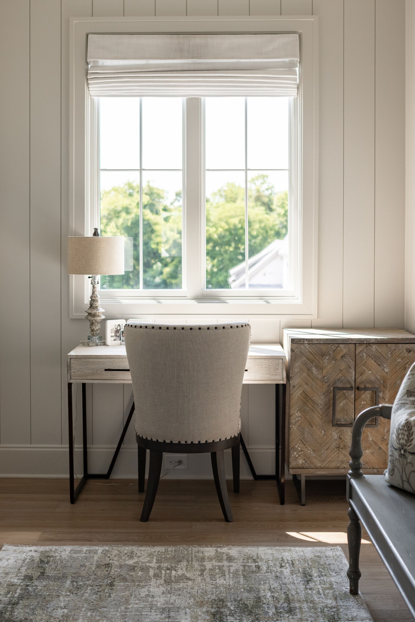 Home office nook with an upholstered chair at a desk beneath a large window.