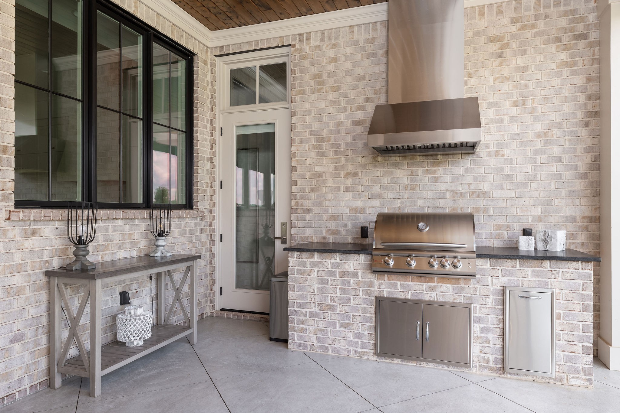 Covered brick patio with a built-in stainless-steel grill, hood, and console table.