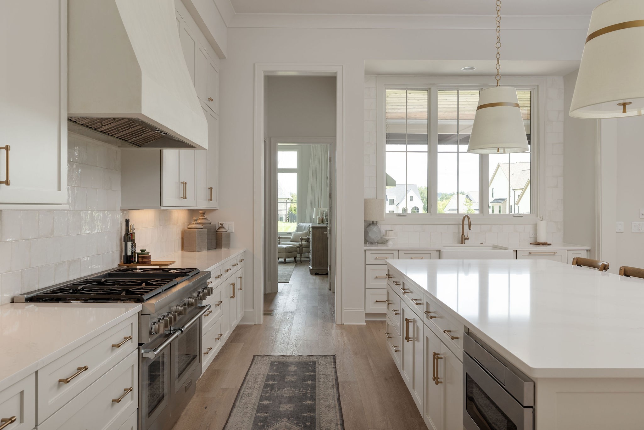 White kitchen with a large island, stainless steel range, brass hardware, and wide windows.