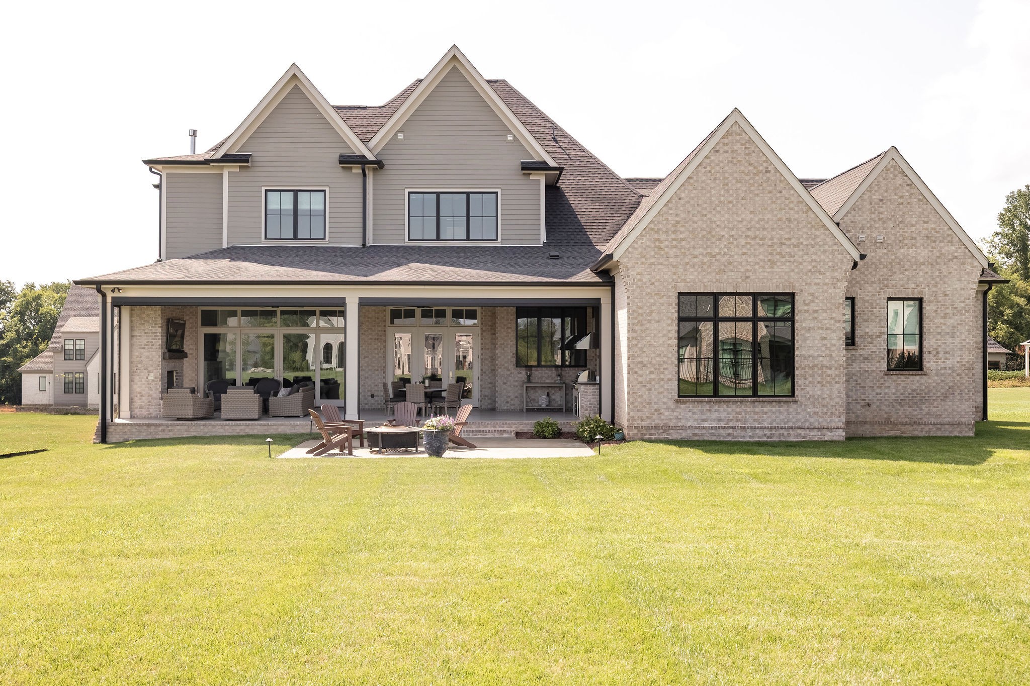 Rear of a two-story home with a covered, furnished patio and broad green lawn.