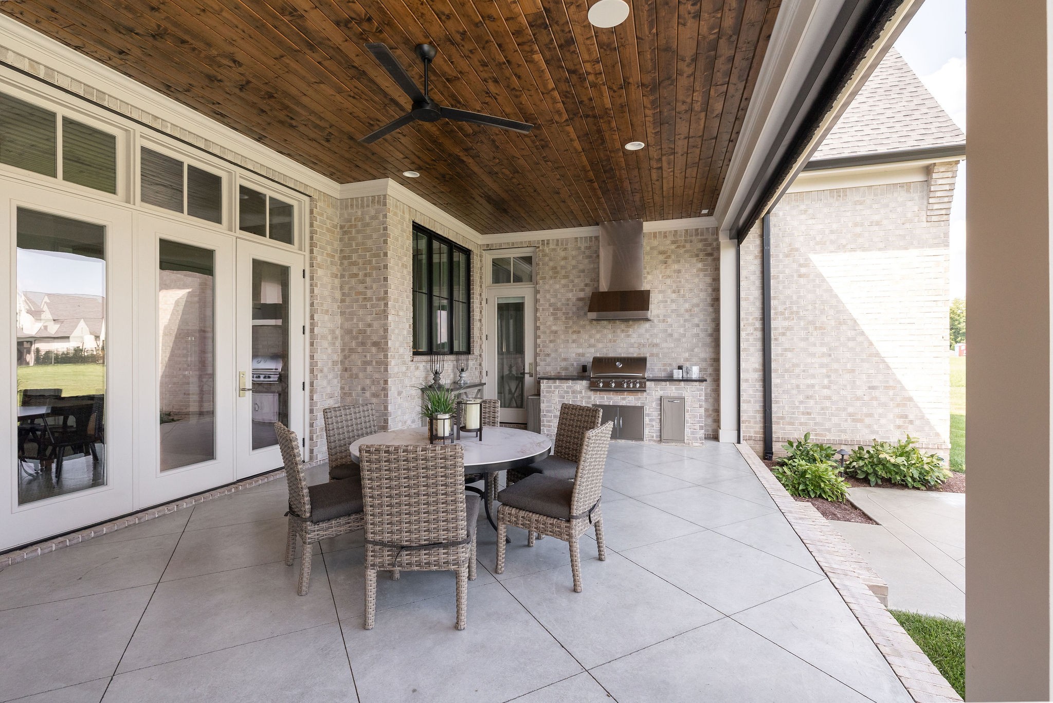 Covered patio with a wood ceiling, wicker dining set, and built-in grill.