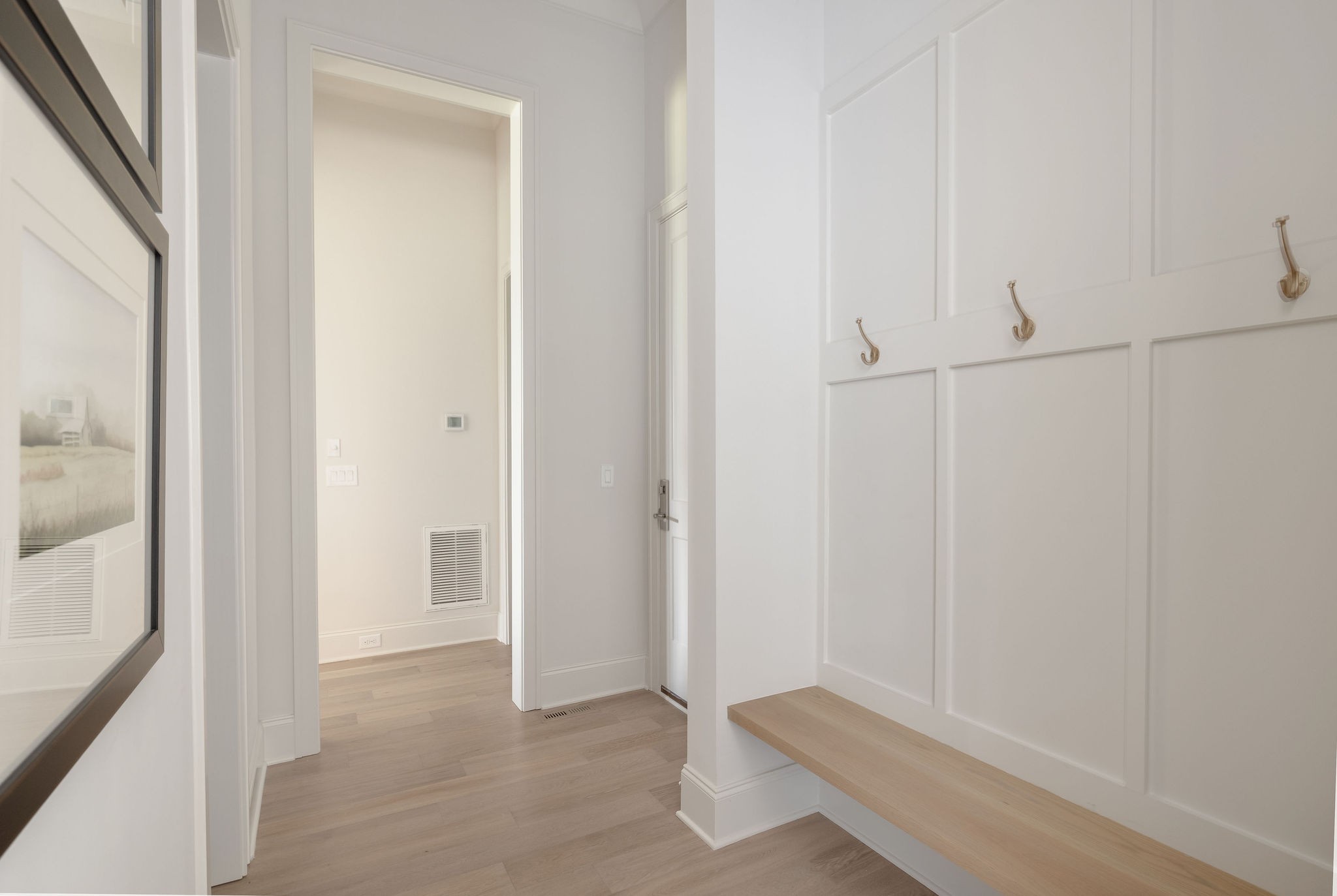 Bright entryway with a built-in bench, brass hooks, light wood floors, and framed artwork.